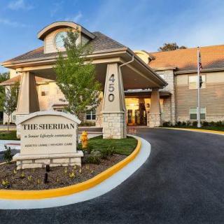 The entrance of a building with a visible sign and landscaped surroundings.