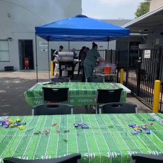 An outdoor party setup with a barbecue station under a blue tent and tables covered with themed tablecloths.
