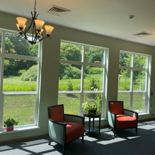 A sunlit lounge area with two chairs by large windows overlooking greenery.