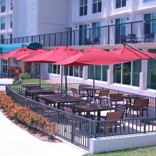 An outdoor restaurant patio with red umbrellas and neatly arranged tables and chairs on a sunny day.