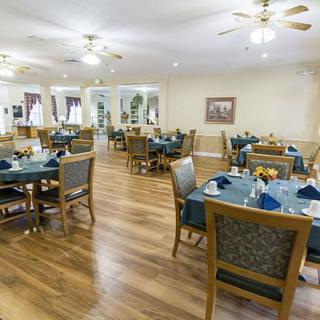 A spacious dining area with neatly arranged tables and chairs, featuring wooden floors and ceiling fans.