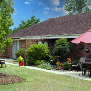 A cozy brick house with a landscaped garden and outdoor patio furniture under a large umbrella.