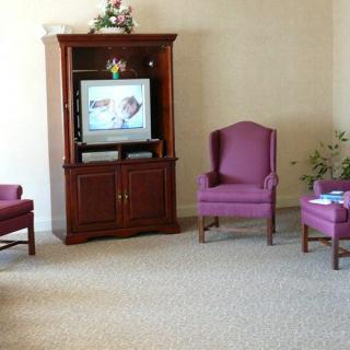 A cozy living room with a television on a wooden entertainment center, surrounded by purple armchairs and a small table.