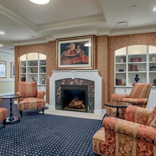A cozy living room with a fireplace, surrounded by comfortable seating and decorated with elegant artwork and bookshelves.