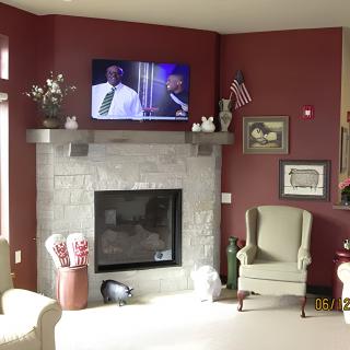 A cozy living room with a stone fireplace and a mounted television, featuring armchairs and decorative elements.