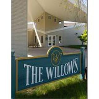 Entrance sign for The Willows with modern building in the background.