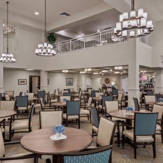 A spacious dining room with multiple tables and chairs, featuring elegant chandeliers.