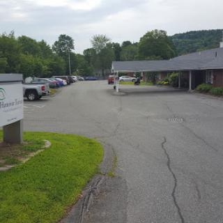 A view of a parking lot and road lined with trees under a cloudy sky.