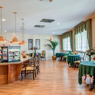 A cozy cafe interior with wooden flooring and green accents, featuring elegantly arranged tables and chairs.
