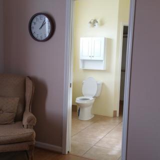 A view from a living room into a bathroom, with an armchair and a wall clock visible.