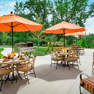 An inviting outdoor patio setup with tables and chairs under bright orange umbrellas surrounded by greenery.