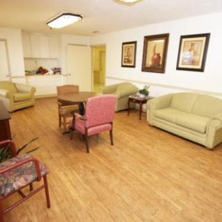 A cozy living room with sofas, chairs, and a wooden floor, decorated with paintings on the wall.