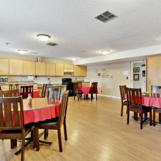 A dining area with multiple tables and chairs, featuring a kitchen in the background.