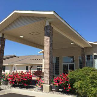 A building entrance with a covered roof and landscaped flowers.