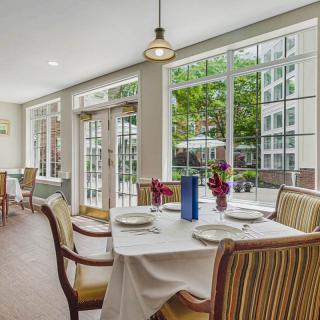 A well-lit dining area with a table set for four, overlooking a garden through large windows.