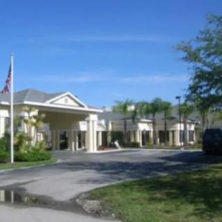 A building with an entrance driveway, surrounded by trees and a flagpole under a clear blue sky.