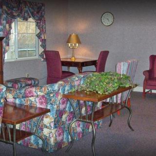 A cozy living room with floral-patterned sofa, burgundy chairs, and a warm table lamp.