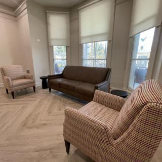 A cozy living room setup featuring a brown sofa and patterned armchairs, illuminated by natural light from large windows.