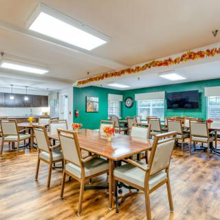 A spacious dining room with multiple tables and chairs, decorated with seasonal accents and equipped with a wall-mounted television.