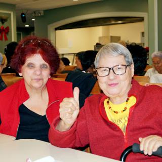 Two elderly women enjoying a moment together, dressed in red and sharing a smile.