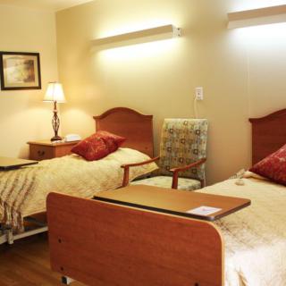 A hospital room with two beds, each equipped with a bedside table and an armchair between them.