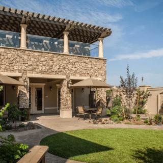 A beautiful stone house with a spacious patio and lush backyard, featuring outdoor seating under umbrellas.