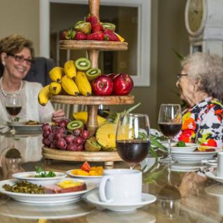 A warm gathering over a beautifully arranged meal featuring fresh fruits and delightful conversation between two seniors.