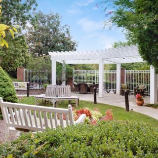 A serene garden with a white pergola, outdoor seating, and lush greenery.