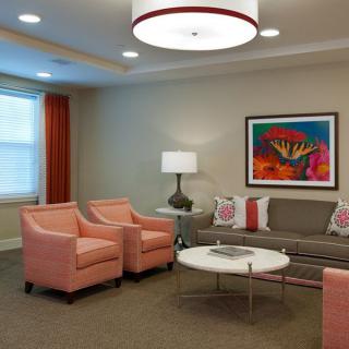 A modern living room with peach armchairs, a gray couch, and vibrant artwork on the wall.