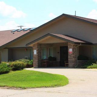 A single-story residential building with a well-kept lawn and a driveway leading to the entrance.