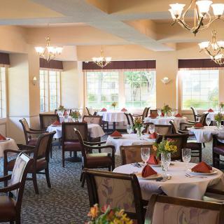 An elegantly furnished dining room with chandeliers and neatly set tables.