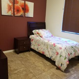 A cozy bedroom featuring a single bed with floral bedding, a nightstand, and decorative artwork on the wall.