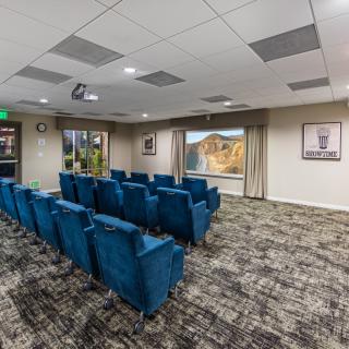 A cozy theater room with blue chairs arranged towards a projector screen.