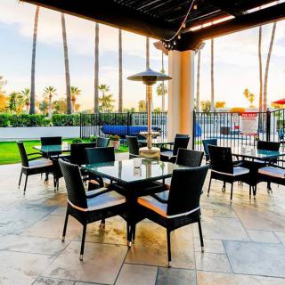 A spacious outdoor patio with elegant seating arrangements under a sunset sky, adorned with palm trees.