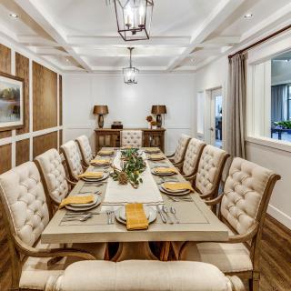 An elegantly designed dining room with a long table set for dinner, featuring upholstered chairs and warm neutral tones.