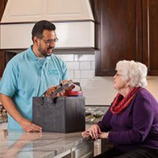 A delivery person brings groceries to an elderly woman in her kitchen.