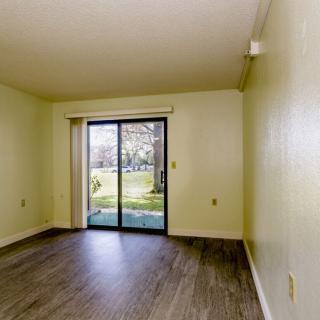 An empty living room with hardwood flooring and a sliding glass door leading to an outdoor area.