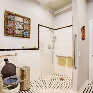 An accessible bathroom featuring a shower, grab bars, and a toilet with black and white tile flooring.