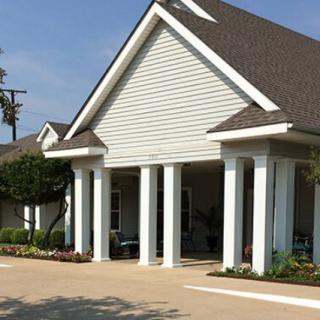 A building with a pitched roof and white columns at the entrance, surrounded by landscaping.