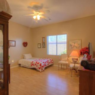 A cozy bedroom with a single bed featuring heart-patterned bedding, illuminated by natural light from a window. The room has warm decor and wooden flooring.
