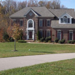 A large suburban brick house with a well-maintained lawn and paved driveway.
