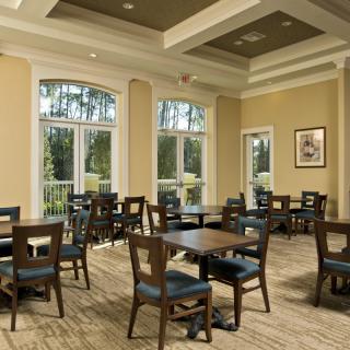 A well-lit dining room with multiple tables and chairs, featuring large windows that let in natural light.