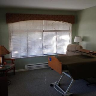 A hospital room with a bed, chair, lamp, and window blinds.