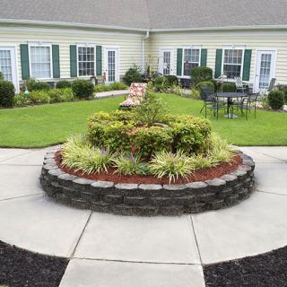 A beautifully landscaped courtyard with a circular arrangement of shrubs and bushes surrounded by pavement.
