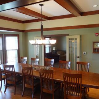 An elegant dining room featuring a long wooden table with matching chairs under a stylish chandelier.