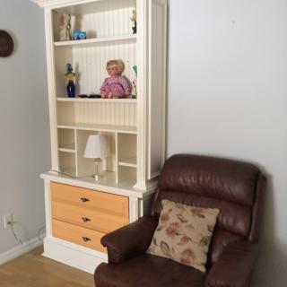 A cozy living room corner featuring a white bookshelf and a brown recliner chair with a floral cushion.