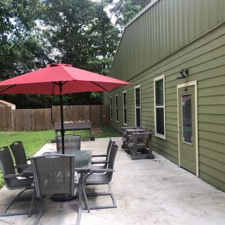 A backyard patio with a table, chairs, and a red umbrella next to a green building.