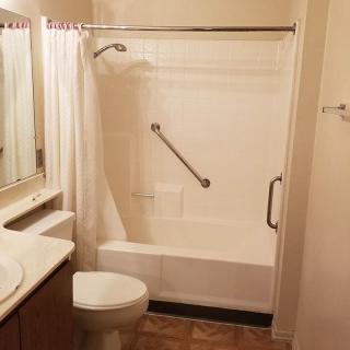 A bathroom featuring a bathtub with shower curtain, toilet, sink, and grab bars for safety.