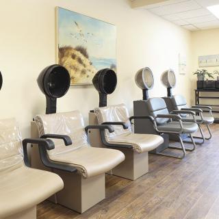 An empty hair salon with a row of chairs and hair dryers along the wall.