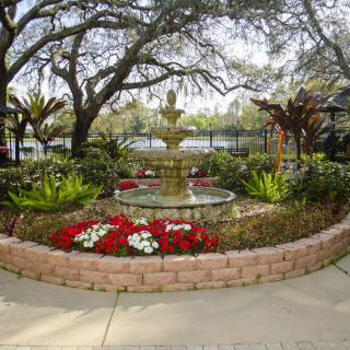 A scenic garden with a central fountain surrounded by flowers and greenery.